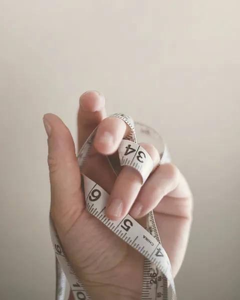 Mano sosteniendo una cinta métrica enrollada sobre un fondo claro