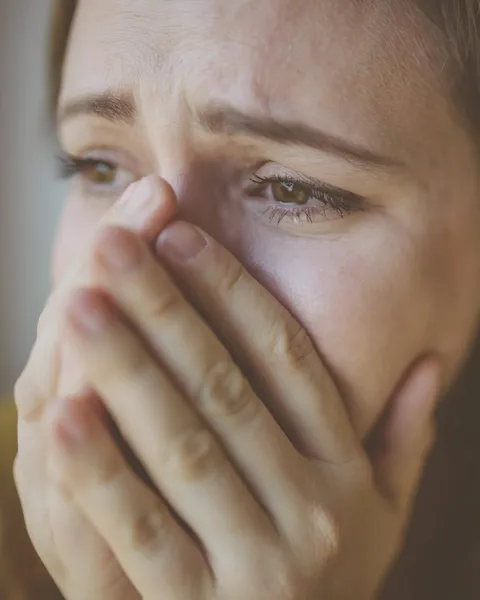 Mujer tapándose la boca con la mano, con los ojos llorosos