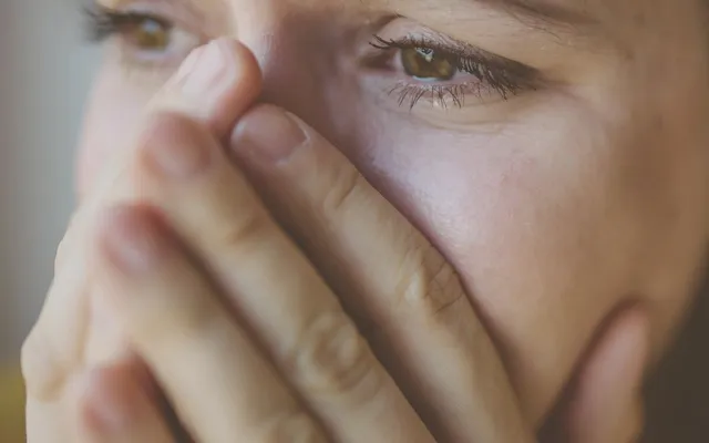 Mujer tapándose la boca con la mano, con los ojos llorosos