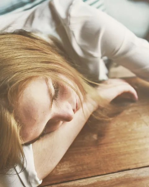 Mujer con la cabeza apoyada en una mesa de madera y los ojos cerrados