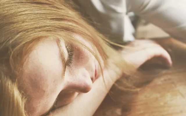 Mujer con la cabeza apoyada en una mesa de madera y los ojos cerrados