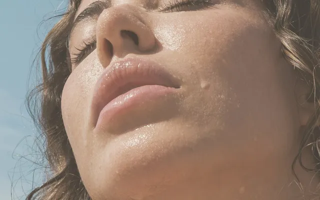 Mujer con la cara vuelta hacia el sol, los ojos cerrados y la piel perlada de sudor