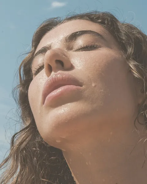 Mujer con la cara vuelta hacia el sol, los ojos cerrados y la piel perlada de sudor